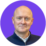 Bald man in a dark blue sweater smiling with a purple background.