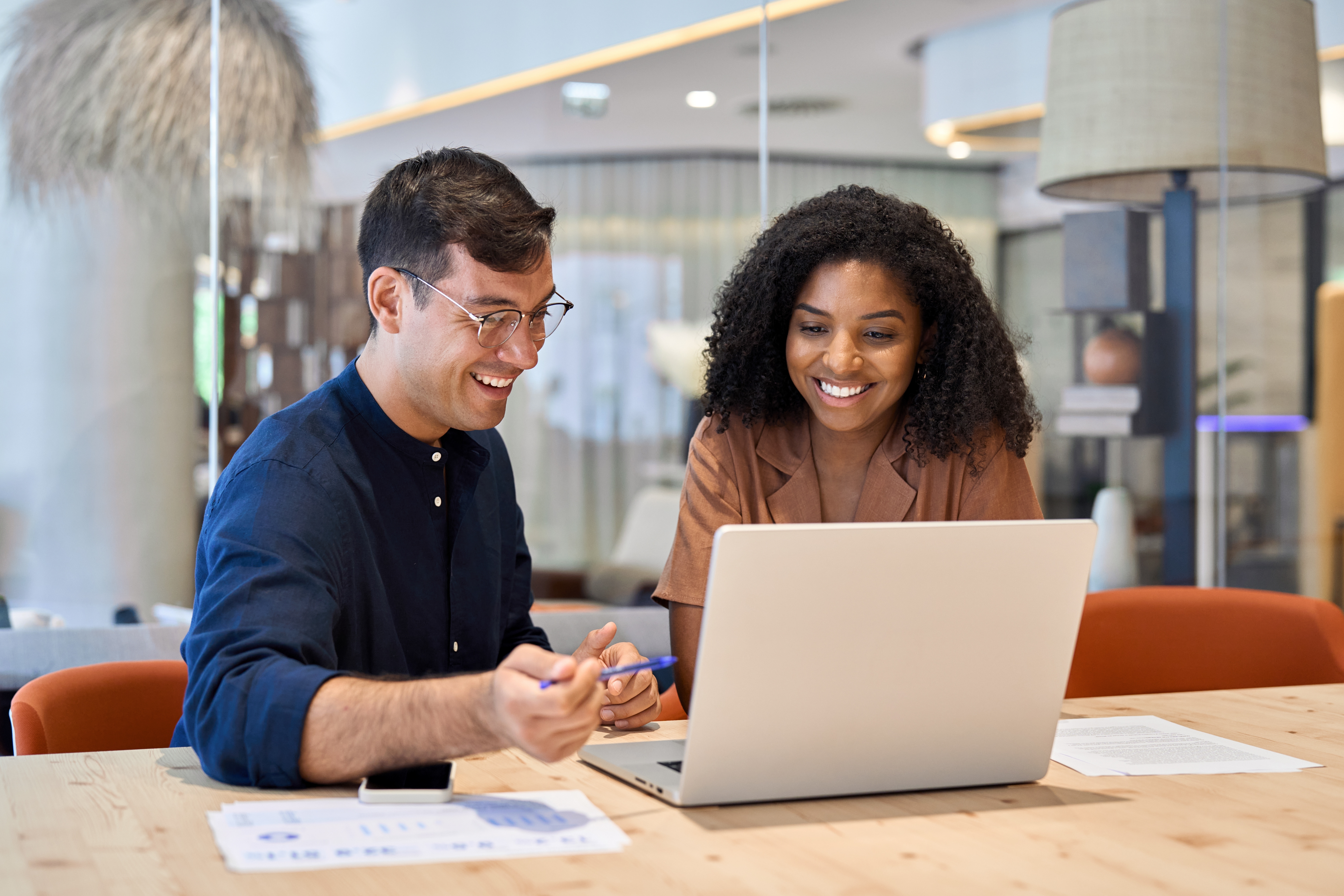A man and a woman sitting in a meeting room looking at a laptop and smiling