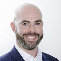 Smiling bald man with a beard wearing a suit and white shirt.