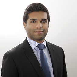 Portrait of a person in a suit and tie smiling slightly against a plain background.
