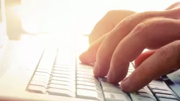 Hands typing on a laptop keyboard in bright light.