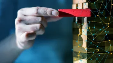 Hand removes a red block from a Jenga tower with digital network overlay.