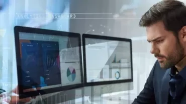 Man analyzing data on multiple computer screens in an office.