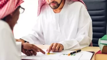 Two men in traditional attire reviewing documents at a desk.