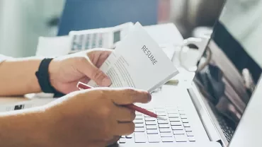 Person reviewing a resume with a laptop and coffee cup on the desk.