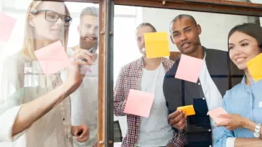 Group of colleagues brainstorming with sticky notes on glass board.