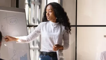 Woman presenting data on a flip chart to colleagues in a meeting room.