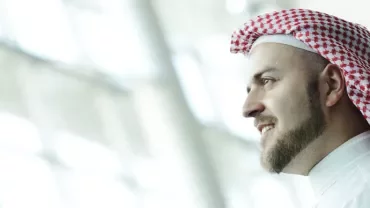 Man wearing a red and white keffiyeh in a bright room.