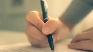Close-up of a hand writing on paper with a pen.