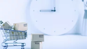 Mini shopping cart with boxes in front of a large clock.