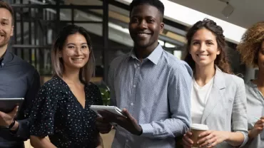 Five people standing in an office, smiling and holding various items.