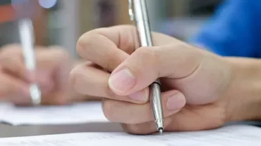 Close-up of a hand writing with a pen on paperwork.