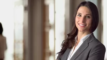 Woman in a business suit smiling with arms crossed in an office.