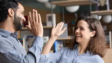 Two people smiling and giving high fives in a library setting.