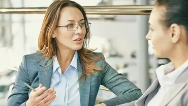 Two businesswomen in conversation in a modern office setting.