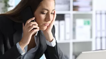 Woman in office speaking on phone and looking at computer.