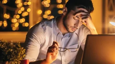 Man looking stressed while working on a laptop by night.