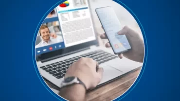 Person using laptop for video call while holding smartphone.