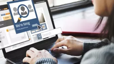 Person using a laptop with a 'We're hiring' pop-up on screen.