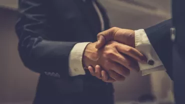 Two business professionals shaking hands in an office setting.