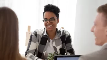 Smiling person in glasses at a desk during a meeting.