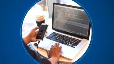 Person working on a laptop while holding a smartphone.