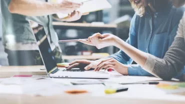 People collaborating at a desk with a laptop and documents.