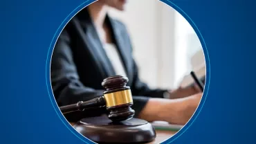 Close-up of a gavel with a person writing in the background, conveying a legal or judicial theme.