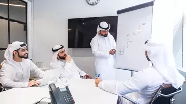 Business meeting with four men in white discussing a graph on a flip chart.