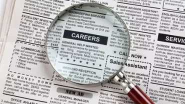 Magnifying glass over newspaper job ads section.