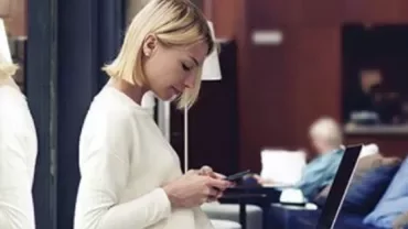 Woman in white sweater using smartphone, seated in a cafe.