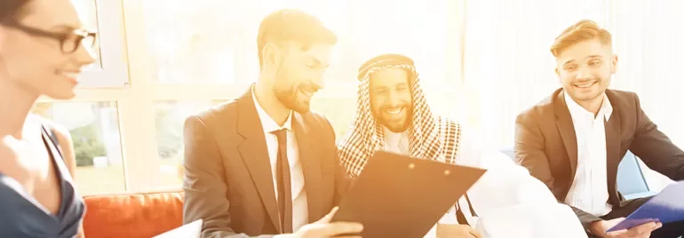 A diverse group of professionals smiling and discussing documents in a sunlit office.
