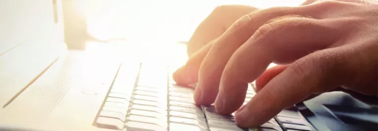 Hands typing on a laptop keyboard in bright light.