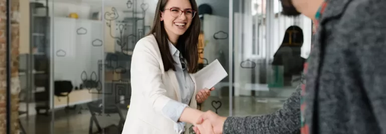 Woman smiling and shaking hands with a person in an office.