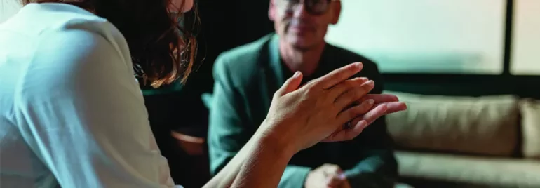 Two people having a conversation in an office setting, one gesturing with hands.