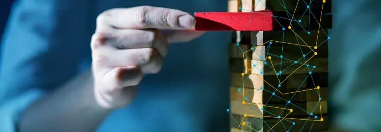 Hand removes a red block from a Jenga tower with digital network overlay.