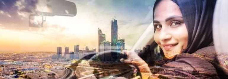 Woman in a headscarf driving with a city skyline in the background.