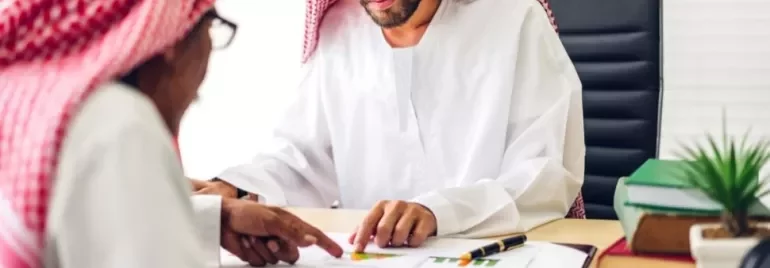 Two men in traditional attire reviewing documents at a desk.