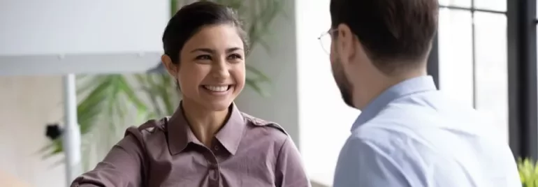 Smiling woman in a purple shirt shaking hands with a man indoors.