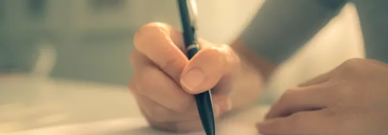 Close-up of a hand writing on paper with a pen.