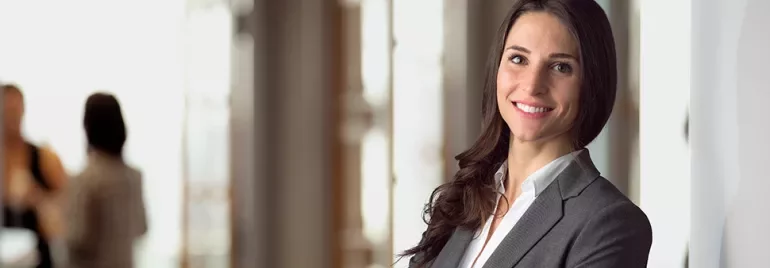 Woman in a business suit smiling with arms crossed in an office.