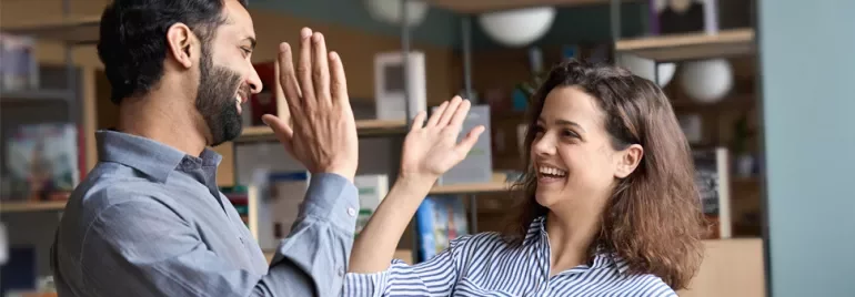 Two people smiling and giving high fives in a library setting.