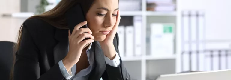 Woman in office speaking on phone and looking at computer.