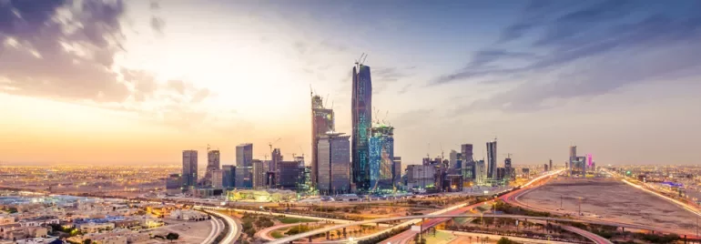 Modern skyline of Riyadh with skyscrapers and a colorful sunset.