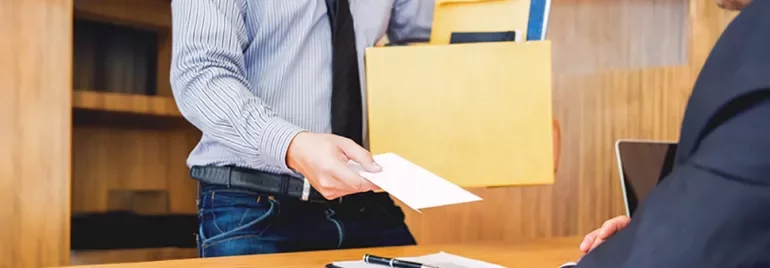 A man in office handing over a resignation letter with a box of his belongings in another hand to the manager sitting. 