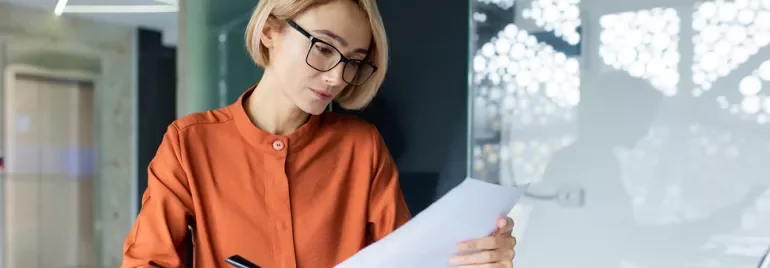 Woman with blonde hair and glasses reading a piece of paper