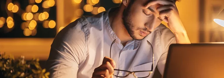 Man looking stressed while working on a laptop by night.