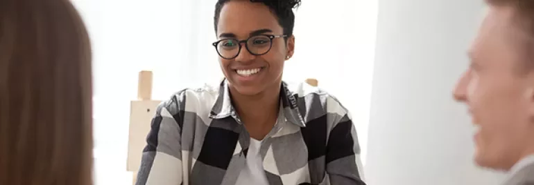Smiling person in glasses at a desk during a meeting.