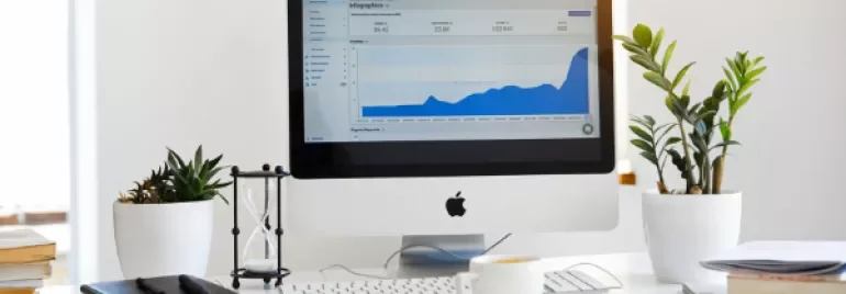 Desktop with a monitor displaying a rising graph, surrounded by plants and office supplies.