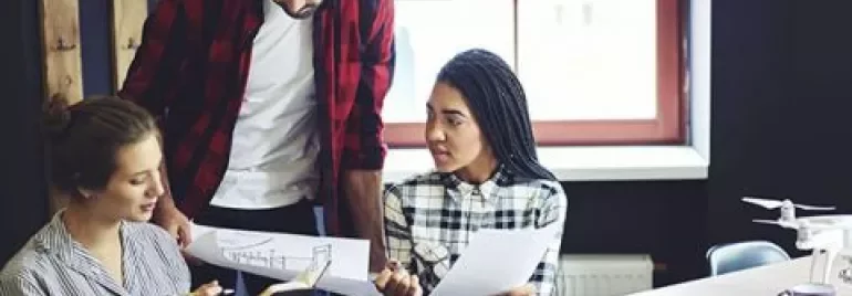 Three people in a meeting room discussing architectural plans around a table.